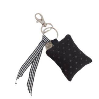 Le Coussin de clé parfumé fève tonka est un porte-clés composé d'un petit coussin noir à pois blancs, d'un ruban vichy noir et blanc, d'une étiquette métallique ronde, d'un fermoir et d'un porte-clés argentés sur fond blanc.