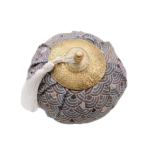 Pochette ronde en tissu à motifs, avec un couvercle texturé en or et un petit bouton sur le dessus, ornée d'un pompon blanc.