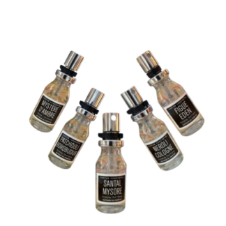 Cinq petits flacons de Parfum d'intérieur concentré - Spray 15 ml avec des étiquettes noires et blanches sont disposés en demi-cercle, chacun affichant un nom de parfum unique comme Santal Mysore et Figue Eden, soulignant leur design élégant.