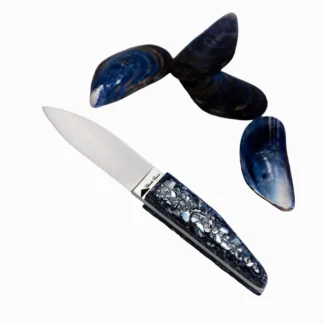 Le Petit couteau à huître - manche coquilles d'huîtres recyclées 13 cm, doté d'une poignée détaillée bleue et argentée, est présenté à côté de trois coquilles de moules bleu foncé sur fond blanc.