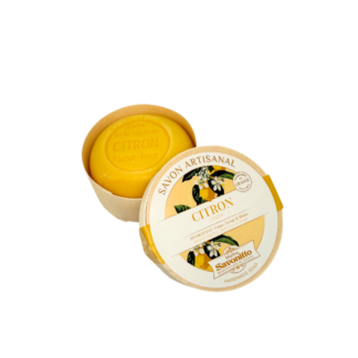 Un savon artisanal au citron Savon -100 g, rond et jaune, se trouve dans une boîte en carton ouverte, ornée de motifs floraux et d'une étiquette "CITRON", mettant en valeur son aspect naturel et artisanal.