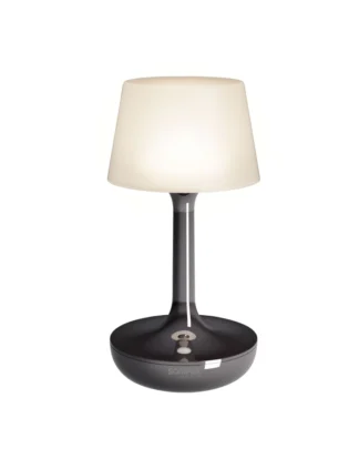 La Lampe GINN est une lampe de table moderne dotée d'une base sombre et brillante, d'un col élancé et d'un abat-jour blanc évasé. Lorsqu'elle est allumée, elle émet une douce lumière blanche.