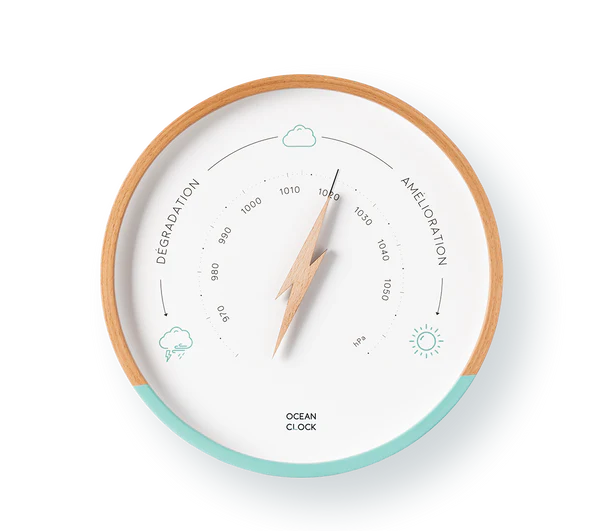 Le Baromètre mural est un baromètre rond avec un cadre en bois et un accent bleu clair. Il comporte une aiguille en forme d'éclair, des icônes météorologiques, la mention "Dégradation" à gauche, "Amélioration" à droite et la marque Ocean Clock en bas.