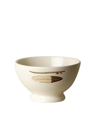 Le Bol Surf vintage est un petit bol de couleur crème avec une courte base sur piédestal et une simple illustration de planche de surf brune sur le côté, sur un fond blanc uni.