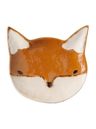 L'Assiette renard amande est un petit plat en céramique en forme de visage de renard, avec une glaçure brun-orange sur le dessus et une glaçure blanche sur le bas du visage et à l'intérieur des oreilles.