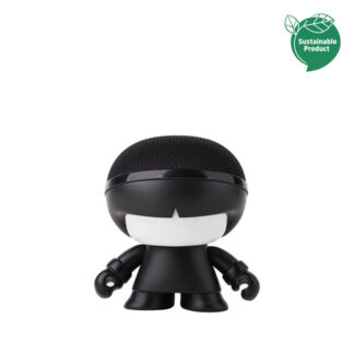 L'Enceinte MINI X BOY est une petite figurine noire en forme de dessin animé, avec une tête ronde, un visage blanc et une calotte noire. De petite taille et compacte, elle porte une étiquette verte "Produit durable" dans le coin supérieur droit.