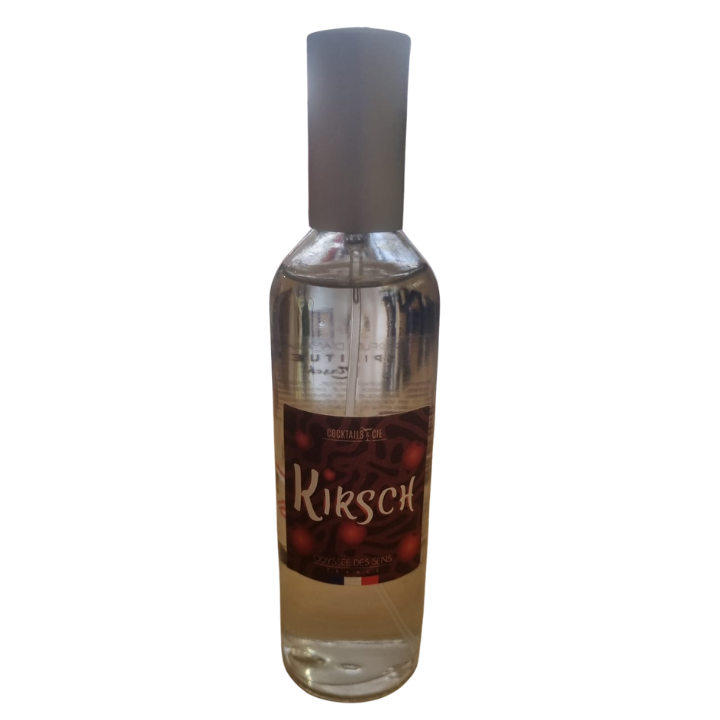 Un flacon en verre transparent étiqueté "Parfum d'ambiance Kir Cassis", présentant des images de cerises sur un fond sombre, avec un bouchon argenté et contenant un liquide transparent.