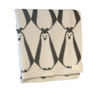 Une laine d'agneau 175x210 (divers coloris) pliée et souple avec un motif répétitif de pingouin noir et blanc sur un fond clair et une petite étiquette en tissu dans le coin.