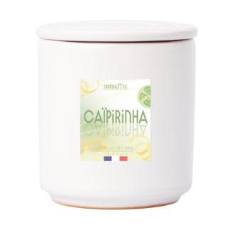 Le cocktail Bougie Caïpirinha est un pot en céramique blanche avec couvercle, étiqueté "Caipirinha" et décoré de tranches de citron vert, du nom de la marque "Cocktails & Cie" et de petites couleurs du drapeau français au fond du pot.