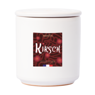 Le cocktail Bougie Kirsch se présente sous la forme d'un pot en céramique blanche avec couvercle, portant l'étiquette "KIRSCH" en gras sur fond rouge avec des illustrations de cerises et un petit drapeau français au fond du pot.