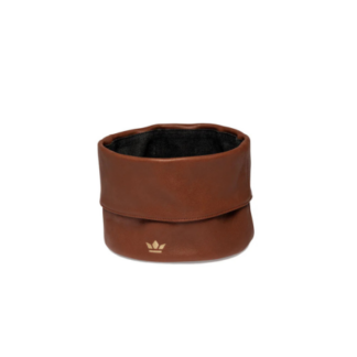 Une Corbeille à pain en cuir marron, ronde avec un bord supérieur plié et un petit emblème doré sur le devant, est présentée sur un fond blanc.
