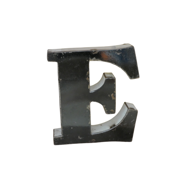 Une grande lettre majuscule noire tridimensionnelle "E" en métal recyclé, d'une hauteur de 15 cm, avec des éraflures visibles et un aspect légèrement usé, rappelant la Lettre E déco métal recyclé, isolée sur un fond blanc.