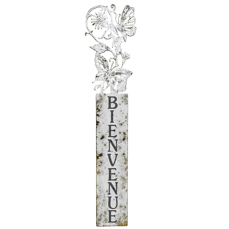 Une grande enseigne rustique en métal avec le mot "BIENVENUE" écrit verticalement en lettres noires et des fleurs décoratives et un papillon au sommet.