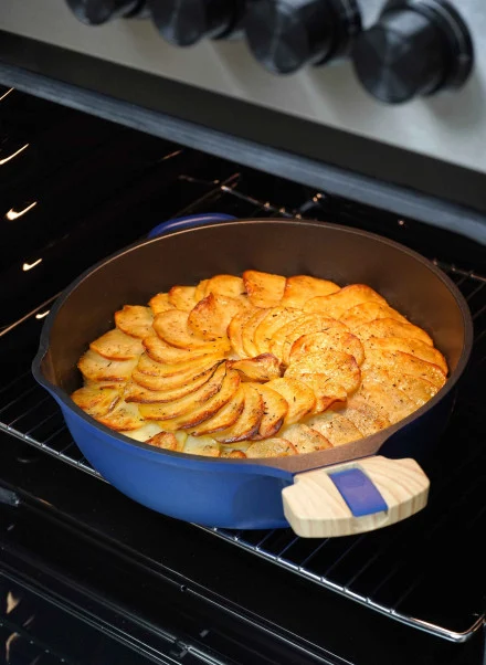 Une Poêle Fabuleuse de 28 cm, remplie de pommes de terre en tranches parfaitement disposées et dorées, cuit sous les boutons noirs du four, sur la grille.