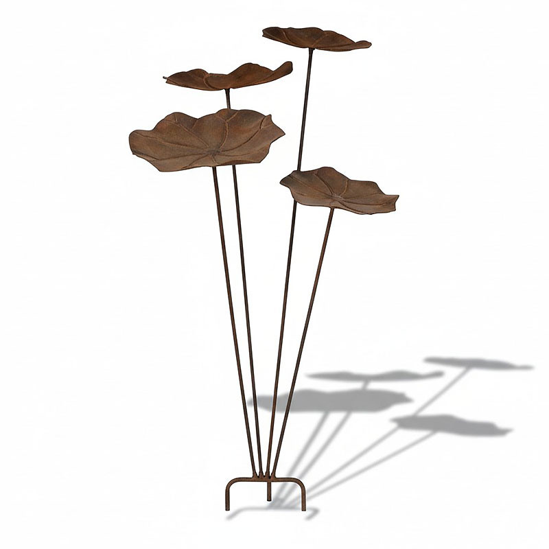 Le Tuteur Nénuphars Jardin est une sculpture métallique composée de quatre formes en forme de feuilles de couleur rouille sur de hautes tiges élancées à différentes hauteurs, projetant des ombres saisissantes sur un fond blanc.