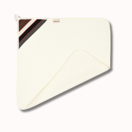 Serviette carrée texturée de couleur crème, dont un coin est replié, avec des rayures diagonales noires, blanches et rouges dans le coin supérieur gauche et une petite boucle en tissu pour la suspendre.