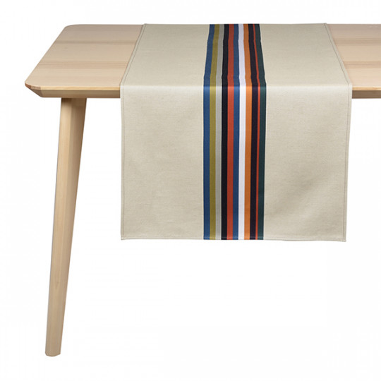 Une table en bois clair avec un chemin de table beige avec des rayures verticales bleu marine, rouge, orange et vert au centre.