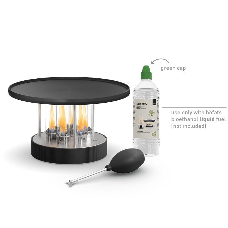 Le CIRCLE 35 au bioéthanol avec plancha – Ø 35 cm – Gril de table höfats présente des flammes visibles sur le plateau, est livré avec un ventilateur noir et est présenté aux côtés d'une bouteille de bioéthanol avec un bouchon vert (carburant non inclus).