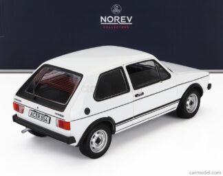 Une voiture miniature Norev Volkswagen Golf GTI 1976 blanche à l'échelle 1/18 est exposée sur une surface unie, avec une boîte de collection NOREV noire en arrière-plan. La voiture présente des finitions noires, des enjoliveurs argentés et une plaque d’immatriculation allemande « AC-RI 854 ».