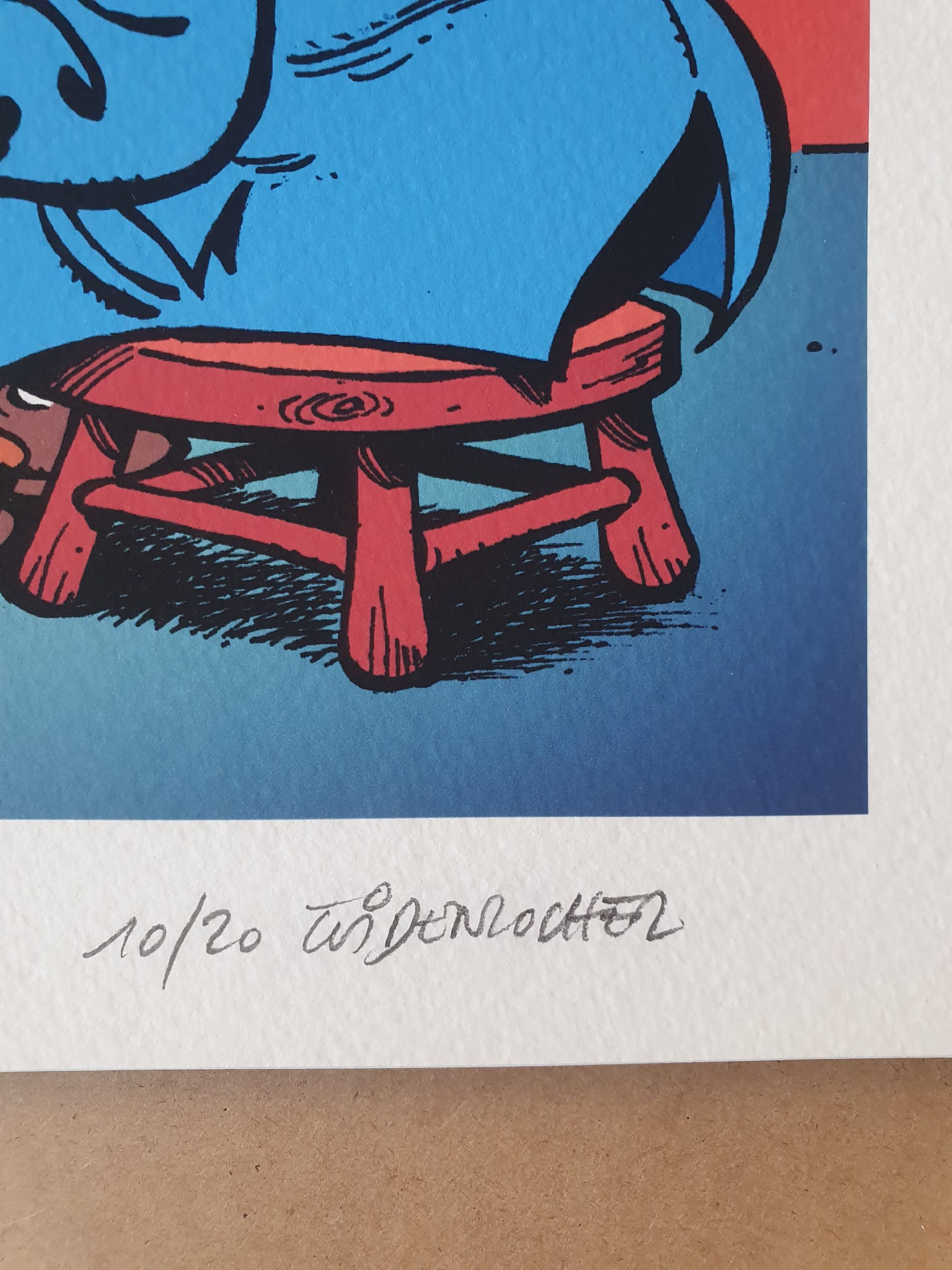 Un gros plan sur le coin inférieur de la lithographie signée Roger Widenlocher - n° 10 « Achille Talon : Le Monde merveilleux » (40 × 50 cm) révèle une signature au crayon et la mention « 10/20 » écrite à la main sous un personnage illustré en bleu, assis sur un tabouret rouge.