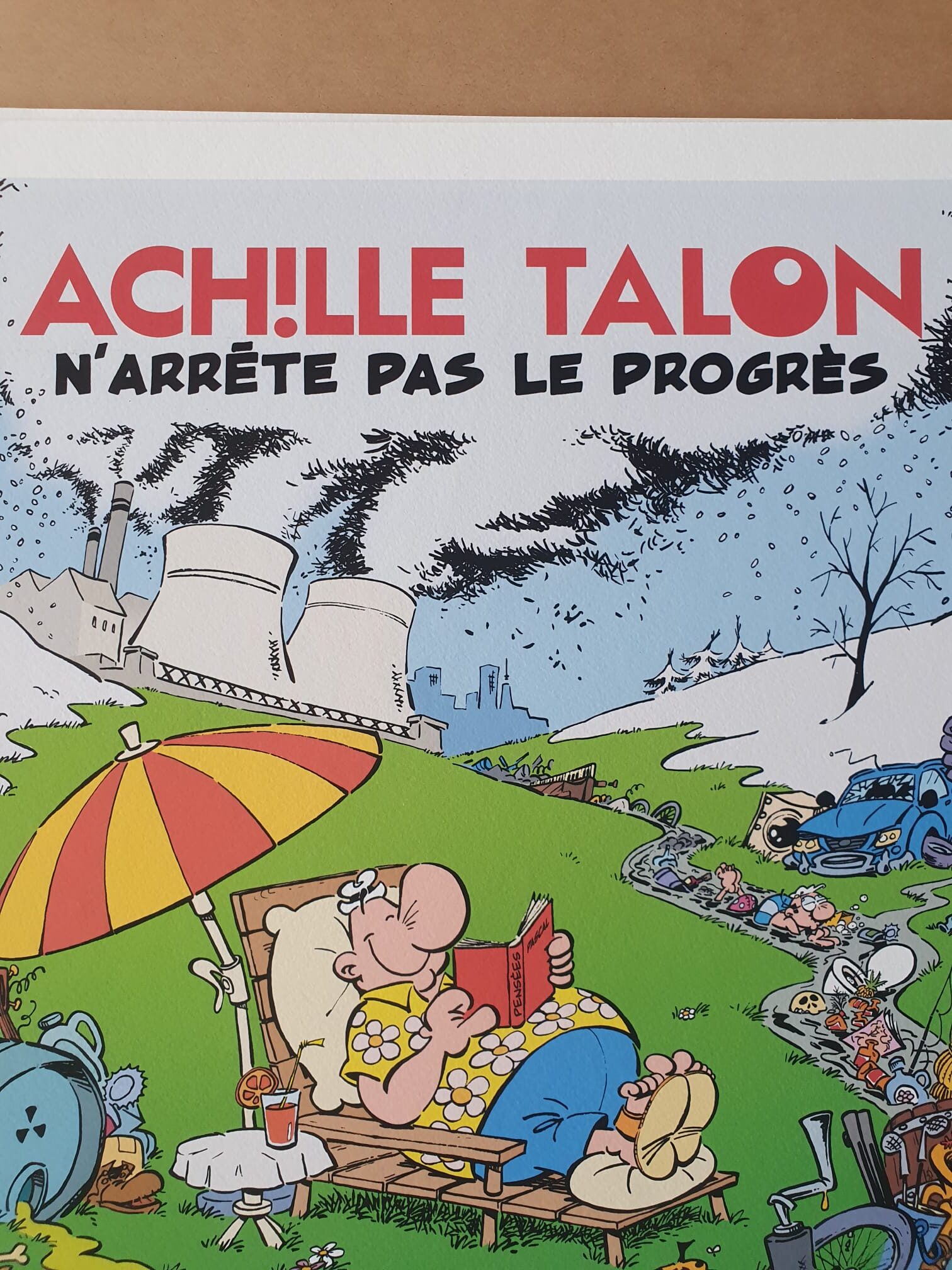 Lithographie Moski – « Achille Talon n’arrête pas le progrès » (40 × 50 cm) : une illustration représentant un homme détendu sur une chaise longue, en train de lire sous un parasol rayé, avec en arrière-plan des usines polluantes et des déchets. Texte : « Achille Talon n’arrête pas le progrès. ».