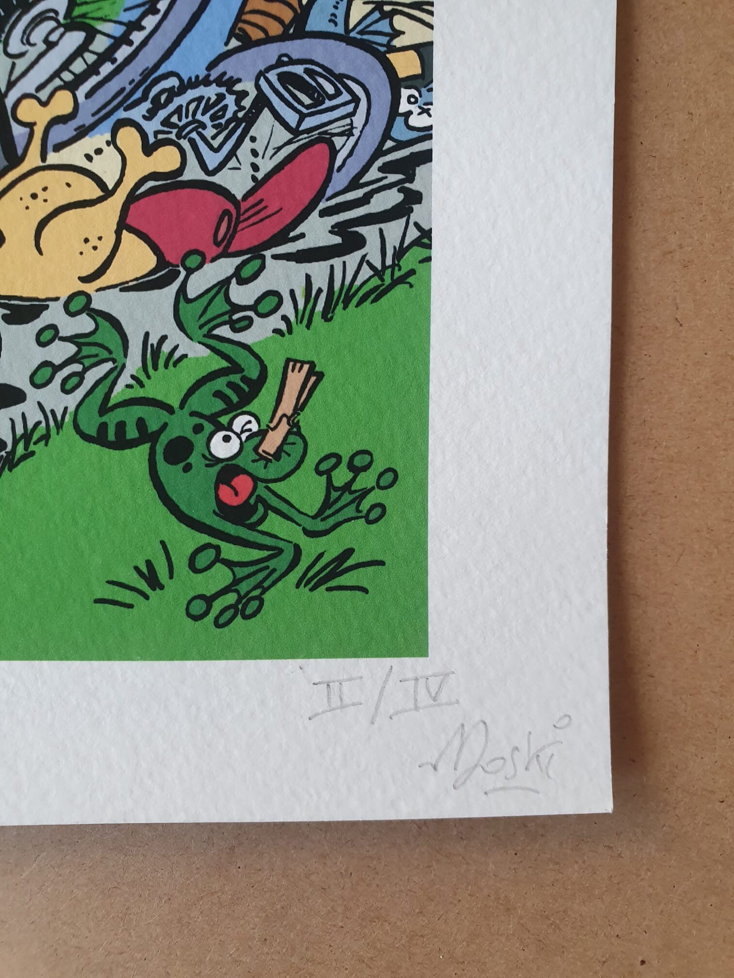 Une lithographie signée intitulée « Lithographie Moski – Achille Talon n’arrête pas le progrès » (40 × 50 cm) représente une grenouille verte caricaturale, parsemée de taches rouges, tenant un bâton dans la bouche. Le papier blanc texturé porte la signature au crayon et la mention d'édition « II/IV » dans un coin, sur un fond de surface marron.