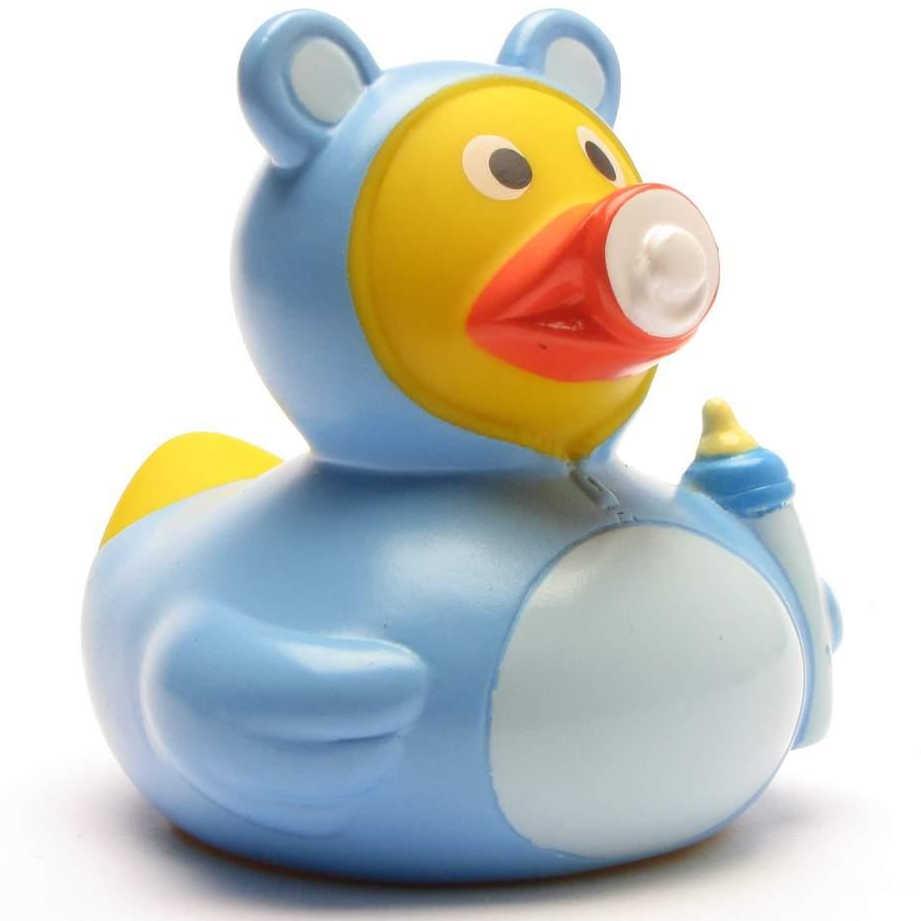 Le « Canard de bain Baby Garçon » est un canard en caoutchouc déguisé en petit garçon, vêtu d'un costume d'ourson bleu, avec une tétine à la bouche et tenant un biberon.