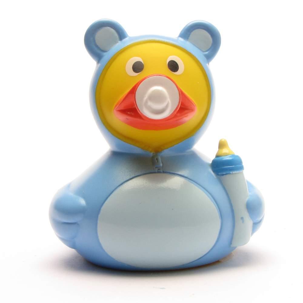 Le « Canard de bain Baby Garçon » est un canard en caoutchouc jaune vêtu d'un costume d'ours bleu, tenant un biberon et ayant une tétine dans la bouche.