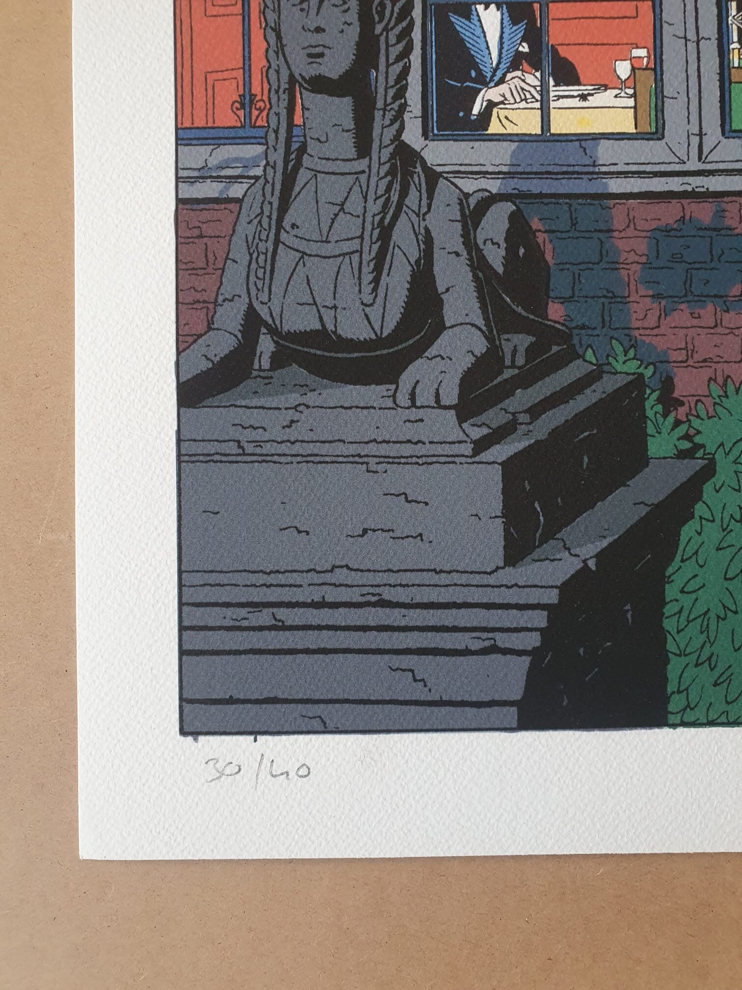 Une lithographie intitulée « Blake et Mortimer : Dîner », réalisée par Ted Benoit (40 × 50 cm), représente une statue de sphinx en pierre devant un mur de briques percé d'une fenêtre, à travers laquelle on aperçoit une personne à l'intérieur d'une pièce. Cette estampe est numérotée à la main au crayon en bas, au numéro 30/40.