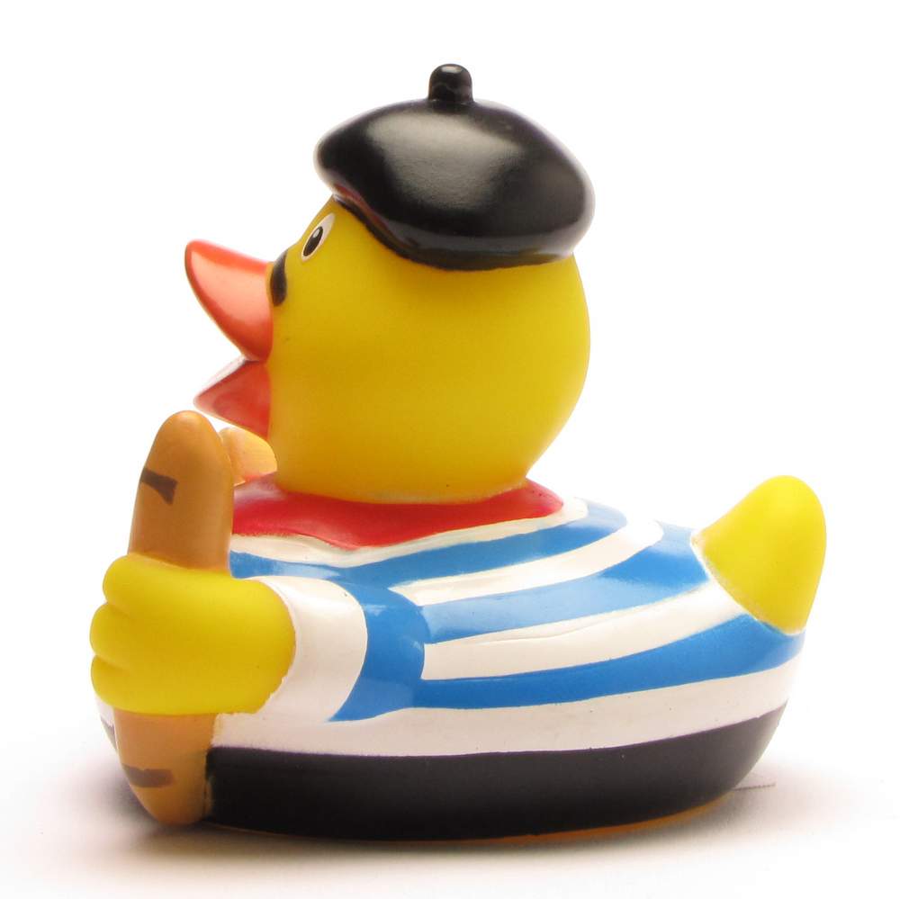 Canard en caoutchouc jaune portant un béret noir, un foulard rouge et une chemise rayée bleue et blanche, tenant une baguette, sur fond blanc.