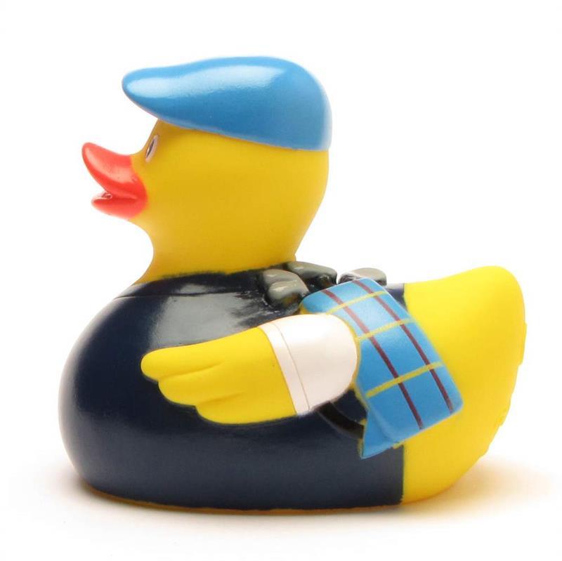 Un canard en caoutchouc jaune porte une casquette bleue, une veste bleu foncé et une écharpe bleue à motifs sur l'aile. Le canard est tourné vers la gauche ; on aperçoit son bec orange vif et son expression espiègle, digne d'un dessin animé.