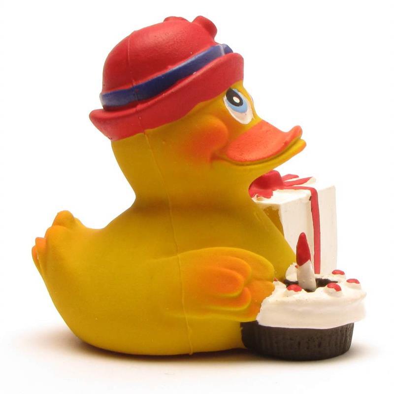 Un canard en caoutchouc jaune, coiffé d'un chapeau rouge, tient dans ses mains un petit gâteau d'anniversaire orné d'une bougie et une boîte-cadeau blanche nouée d'un ruban rouge.