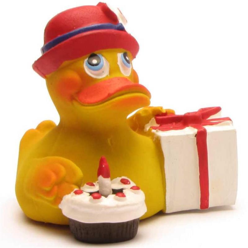Un canard en caoutchouc jaune coiffé d'un chapeau rouge tient un paquet cadeau blanc orné d'un ruban rouge et est assis à côté d'un petit gâteau sur lequel brûle une bougie.