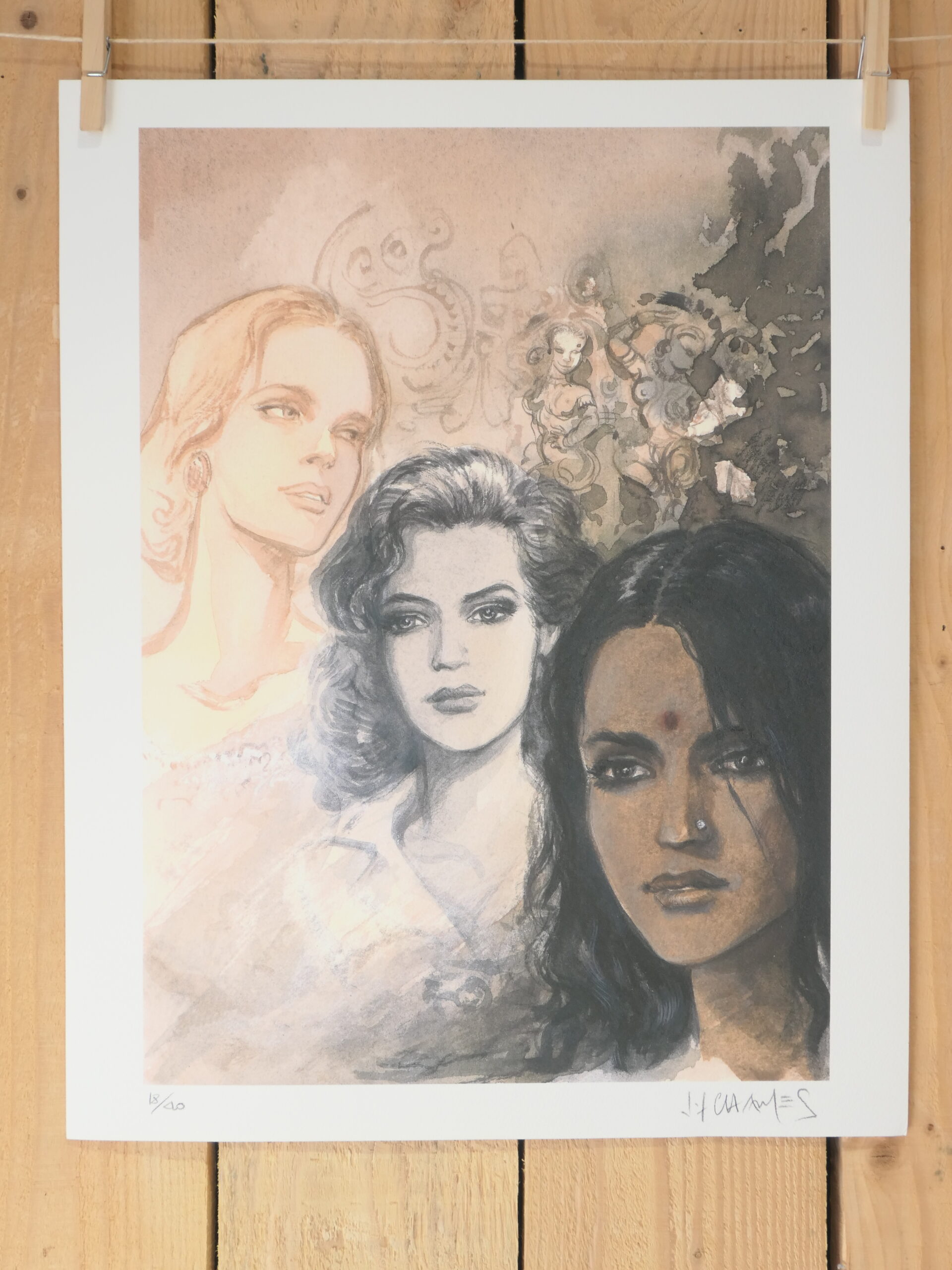 « Lithographie Jean-François Charles – Visages » est une reproduction artistique de 40 × 50 cm représentant trois visages de femmes aux teints de peau variés et aux expressions sérieuses, sur un fond de style aquarelle orné d'éléments floraux. La reproduction est présentée fixée sur un mur en bois.