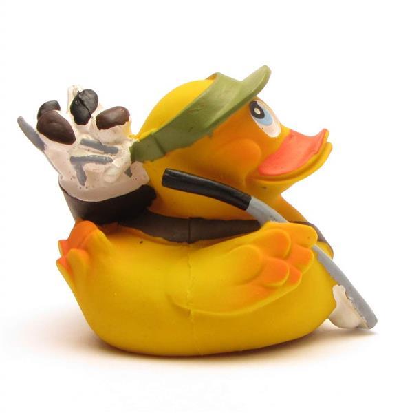 Un canard en caoutchouc jaune déguisé en golfeur, coiffé d'une visière verte, tenant un club de golf et portant un sac de golf rempli de clubs sur l'épaule.