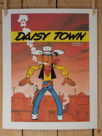 Lucky Luke, un cow-boy de bande dessinée, se tient debout devant une ville de l’Ouest, sous un ciel rouge, les mains posées le long du corps. La fumée de sa cigarette s'enroule au-dessus de lui en formant des crânes, avec l'inscription « Daisy Town » au-dessus de sa tête. Cette illustration figure sur la lithographie « Lithographie Morris – Lucky Luke : Daisy Town – 40 × 50 cm ».
