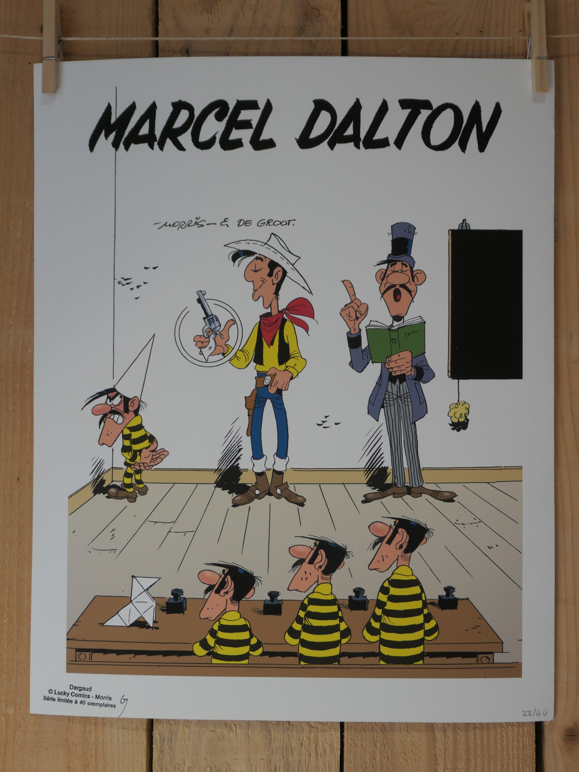 Lithographie Morris – Lucky Luke : Marcel Dalton (40 × 50 cm) : Dessin représentant quatre prisonniers vêtus d’un uniforme rayé noir et jaune, assis à des pupitres dans une salle de classe, sous le regard d’un shérif et d’un professeur, avec la mention « Marcel Dalton » inscrite en haut de l’illustration.