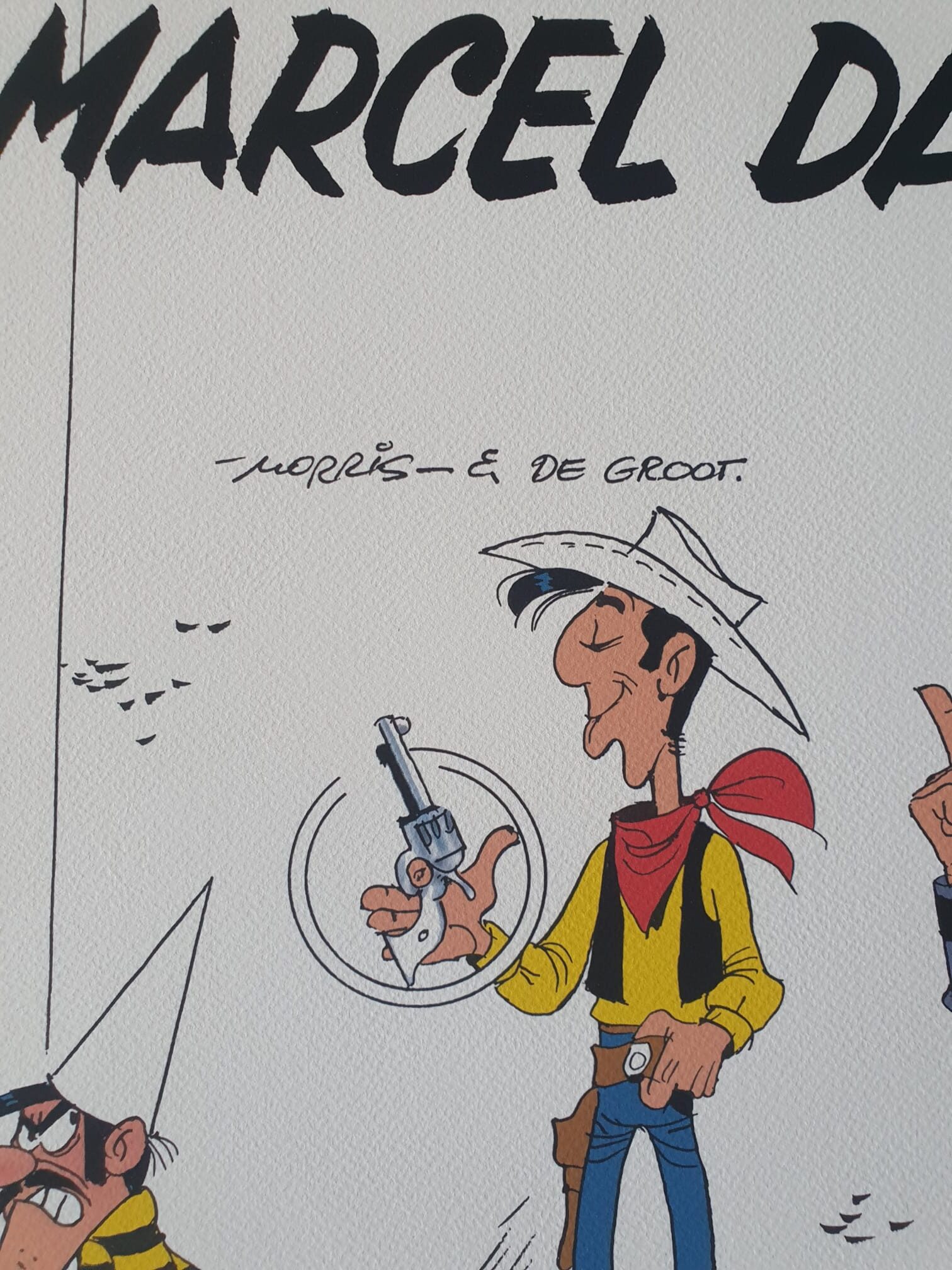 Voici une version réécrite à partir des données de votre produit : un cow-boy de bande dessinée — Lucky Luke, tiré de « Lithographie Morris – Lucky Luke : Marcel Dalton – 40 × 50 cm » — porte une chemise jaune, un foulard rouge et un chapeau blanc, tout en faisant tournoyer un revolver. Au-dessus de lui figure un texte en noir, avec deux signatures (« Morris » et « de Groot ») à proximité ; une partie d’un autre personnage de bande dessinée apparaît sur le bord gauche.