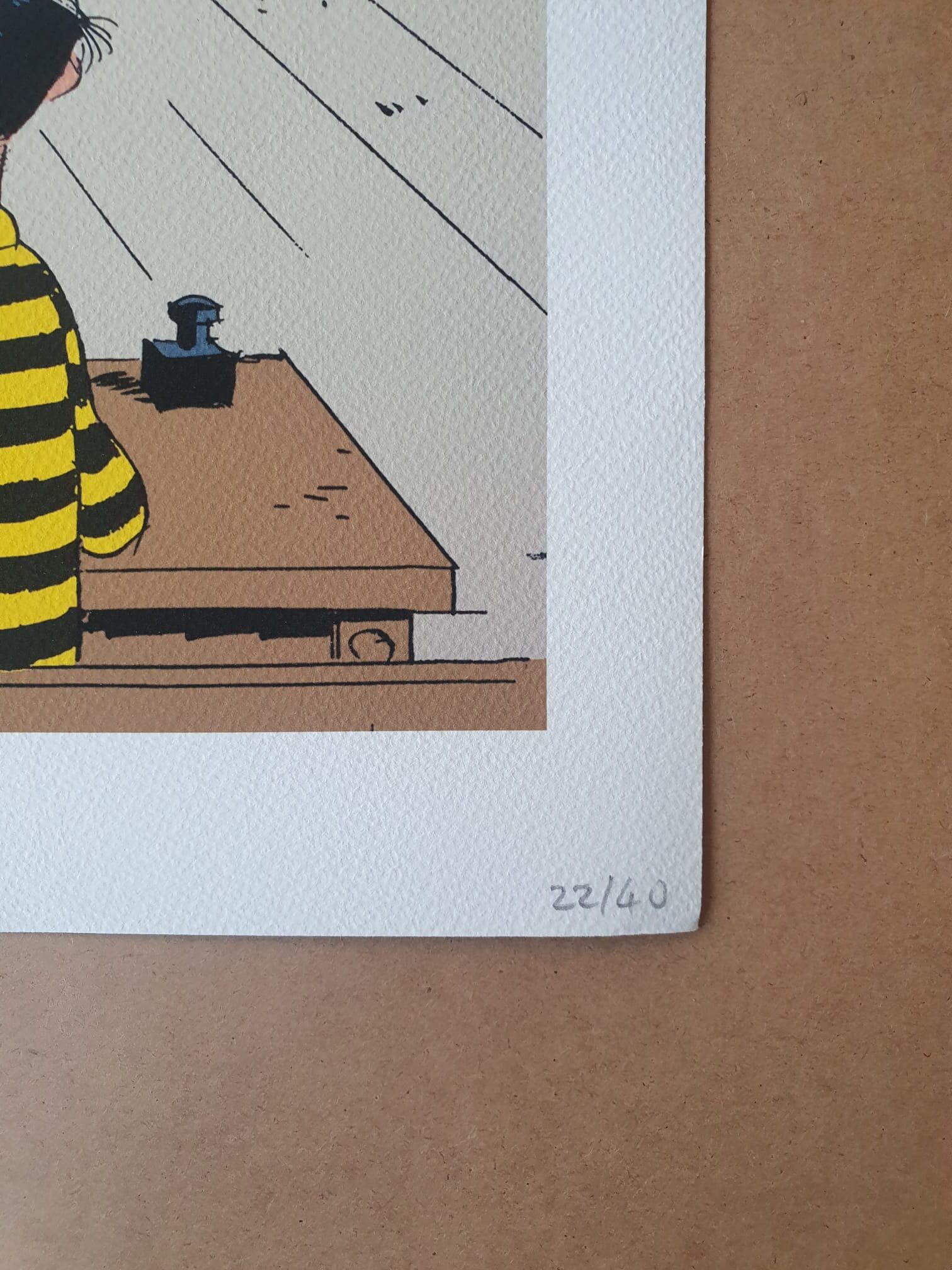 Bien sûr ! Voici une version remaniée de votre phrase en utilisant les données du produit fournies : « Illustration partielle d’un personnage vêtu d’un t-shirt rayé jaune et noir, assis à un bureau, tirée de la « Lithographie Morris – Lucky Luke : Marcel Dalton – 40 × 50 cm », l’œuvre étant numérotée 22/40 au crayon sur du papier blanc texturé, sur fond marron. ».