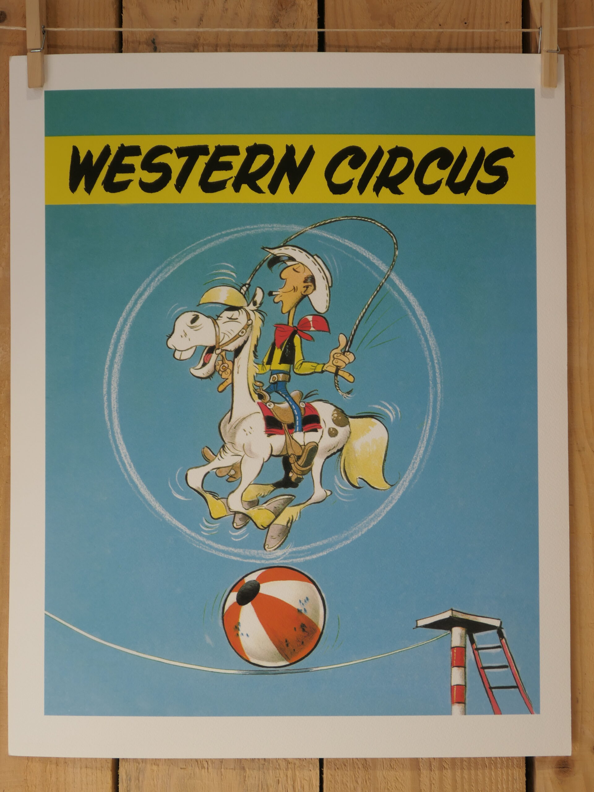 Bien sûr ! Voici une phrase réécrite à partir des informations fournies sur le produit : Une lithographie de Morris représentant Lucky Luke, intitulée « Western Circus » (40 × 50 cm) : Lucky Luke, le cow-boy de bande dessinée, chevauche un cheval blanc tandis que tous deux se tiennent en équilibre sur un ballon de plage à l'aide d'un lasso, sous l'inscription « Western Circus » sur fond bleu. Une piste de cirque est visible dans le coin inférieur.