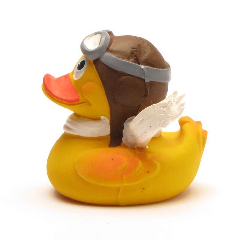 Un canard en caoutchouc jaune portant des lunettes d'aviateur, un casque de pilote marron, une écharpe blanche et de petites ailes blanches, tourné vers la gauche sur un fond blanc.