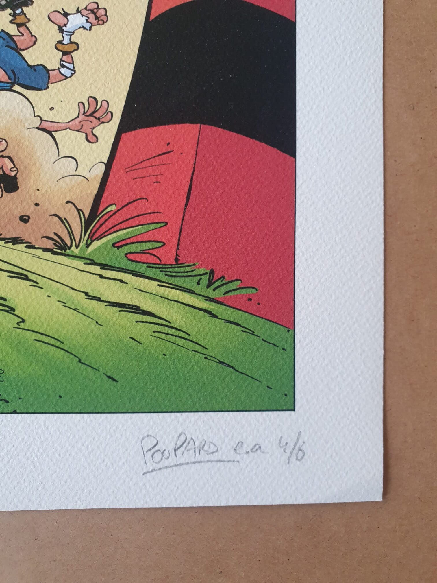 Un gros plan de la lithographie « Jean-Charles Poupard – Rugby 2 » (40 × 50 cm) montre un coin dessiné dans un style bande dessinée, comportant des fragments d'un objet rouge et noir, de l'herbe verte et une main accompagnée de la signature manuscrite « Poupard e.a 4/6 » sur du papier blanc texturé.