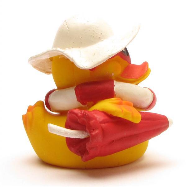 Un canard en caoutchouc jaune portant un chapeau de soleil blanc, des lunettes de soleil rouges et un gilet de sauvetage blanc et rouge, tenant un parapluie rouge fermé.