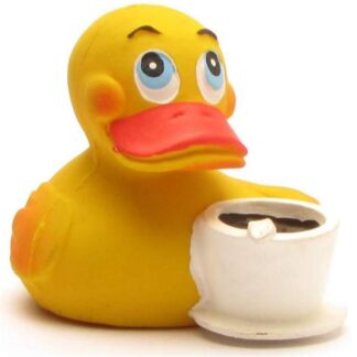 Un canard en caoutchouc jaune aux grands yeux bleus tient une tasse à café blanche remplie d'un liquide foncé et d'une guimauve ; il a l'air joyeux et espiègle.