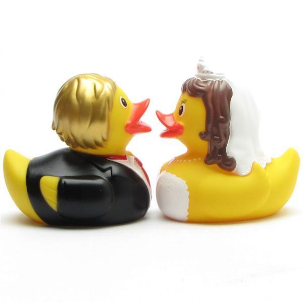 Deux canards en caoutchouc déguisés en mariés se font face. Le canard marié porte un costume et a les cheveux blonds, tandis que la canarde mariée porte une robe blanche et un voile, et a les cheveux châtains.