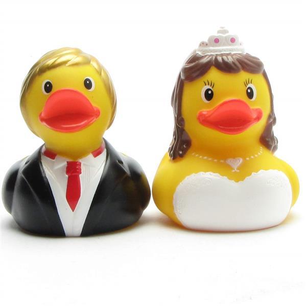 Deux canards en caoutchouc déguisés en mariés. Le canard marié porte un costume et une cravate rouge, tandis que la canarde mariée porte un diadème, un collier et une robe blanche.