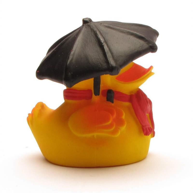 Un canard en caoutchouc jaune, portant une écharpe rouge, tient un parapluie noir ; il est assis sur une surface blanche, dos à l'appareil photo.