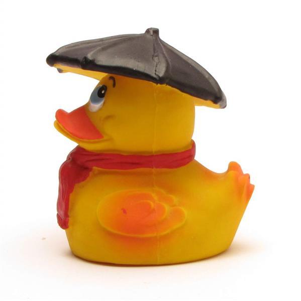 Un canard en caoutchouc jaune portant une écharpe rouge et un chapeau noir en forme de parapluie, tourné vers la gauche, sur fond blanc.