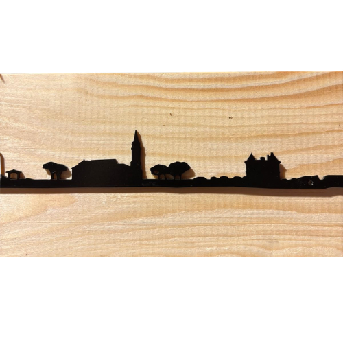 Panneau mural « Skyline » d’Andernos-les-Bains en métal noir de 30 cm représentant la silhouette noire d’un village avec des arbres, un clocher ou une tour et des maisons, sur un fond en bois clair au grain apparent.