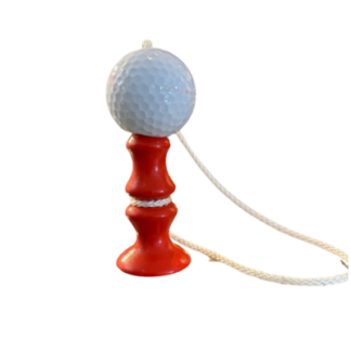 Une balle de golf orange attachée à une ficelle, posée sur un petit support en bois rouge, photographiée en plan large sur fond blanc.